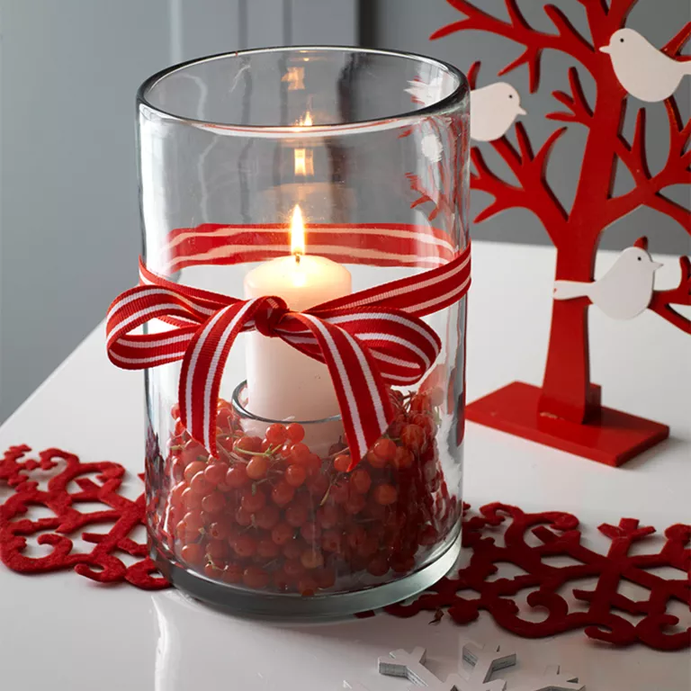 Commencez par mettre un petit gobelet dans un grand vase en verre. Placez une bougie pilier à l'intérieur du gobelet, puis entourez la base du vase avec des canneberges rouges de Noël. Terminez avec une longueur de ruban rayé enroulé autour de l'extérieur et noué en un nœud.